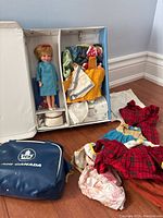 Wide shot showing Penny Brite doll in original box, assorted doll clothes spread on floor, and small blue Air Canada bag.