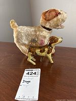 Two vintage wind-up toy dogs positioned on a table, plush dog larger in background and metal dog in front.
