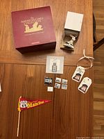 Overview photo of all items including the maroon box, ceramic deer figurine, doll tags, miniature photos and camera, and the Route 66 pennant flag.