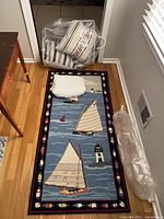 Photo showing four off-white pillows with red and blue stripes packed in a plastic bag on floor, white folded sheet on decorative sailboat-themed rug