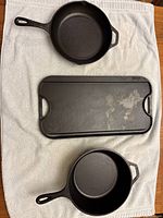 Top view of two Lodge cast iron skillets and one rectangular reversible grill/griddle placed on white towel.