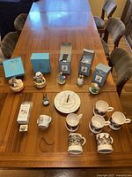 Full set of all items displayed on wooden table: 7 Beatrix Potter figurines with boxes, musical figurines identifiable, Beatrix Potter clock, Peter Rabbit mug, and Emma Bridgewater mugs.