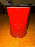 Front view of the red Le Creuset utensil crock showing the embossed brand name and glossy ceramic finish.