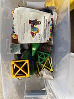 Clear bin filled with various colored Magna-Tiles plastic magnetic tiles including squares and triangles, with paper instruction sheets on top