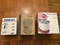 All three boxed appliances placed side by side: Cuisinart Mini-Prep Plus food processor, Citri-Star juicer, KitchenAid ice cream maker attachment.