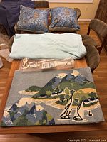 Two blue deer-themed pillows sitting on a couch with a light blue fleece blanket and two seaside-themed rugs laid out flat on a table.