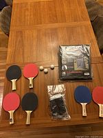 All items displayed on wooden table: 6 paddles (2 Franklin basic and 4 Stiga higher quality), 3 ping pong balls, Kettler net and premium outdoor table tennis cover in original packaging