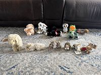 Full lot of 16 stuffed animals including 8 TY brand and 8 Steiff German collectible stuffed animals displayed in line on carpeted surface, showing variety of animal shapes and colors.
