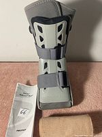 Aircast ankle brace with two wide straps, beige elastic bandage, and instruction manual on surface.