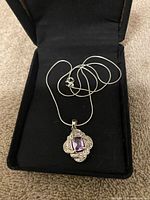 Silver necklace in black jewelry box showing amethyst pendant.
