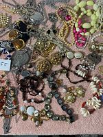 Photo showing a variety of vintage costume jewelry pieces including earrings, bracelets, necklaces, and brooches laid out on a pink cloth.