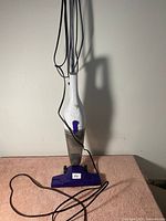 White and purple electric mop cleaner with clear water tank, power cord coiled on floor.