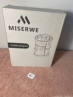 Photo of the MISERWE cosmetics storage box in its retail packaging, showing brand name and a line drawing of the rotary multi-compartment organizer.