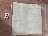 Folded white ladies shirt with floral embroidery and buttons, placed on a pink surface with a small number label '63'.