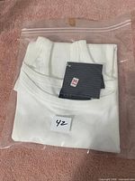 Two white ladies T-shirts, size 42, packed in resealable plastic bags and placed on a pink surface.