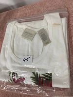 White ladies' T-shirt folded, showing brand tag 'First Issue' with size 45 and leaf print visible in packaging.