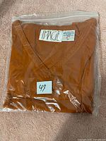 Brown V-neck ladies t-shirt folded and sealed in clear plastic with a label '49' on it.