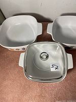 Three square bowls, two with fruit artwork, one plain, and one glass lid shown from front.