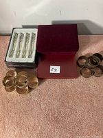 Photo showing 4 vintage metal fruit forks in original plastic packaging with decorative handles and a group of 8 round vintage metal napkin rings.
