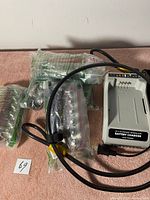 Items on pink surface including a gray battery charger, sealed cables, and black security cable lock.