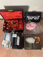 Photo showing wooden jewelry box with red velvet interior and assorted jewelry, Swag eyeglass case, Ammunition power supply, and boxed heart-shaped trinket box.
