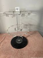 Full view of the two-tier revolving acrylic jewelry display stand on a pink surface