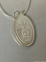 Close-up of oval pendant featuring Asian character and 925 silver mark, showing material and finish.
