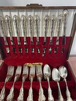 Top-down view of the cutlery set showing knives, forks, and spoons held in slots within the wooden case with red velvet lining.