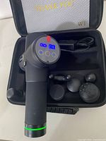 Top view of the massage gun with LED display lit and six attachments inside carrying case