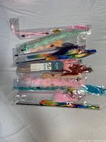 Photo showing the bundle of 10 individual cat toys in plastic packaging, laid out flat on a white surface. Various ribbons and fluffy attachments are visible in multiple colors such as rainbow, mint green, pink, blue, and red.