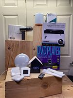 Overview of lot items including the handheld vacuum, two DVD player boxes, birdhouse alarm clock, digital alarm clock, essential oil diffuser, and magnetic lights.