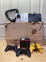 Photo of gaming controllers, security camera, Bluetooth neck speaker, wireless chargers, converters, and TV antenna laid out on wooden block