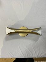 Top-down view of the gold wall sconce, showing its double curved trumpet-shaped arms and central circular mounting plate.