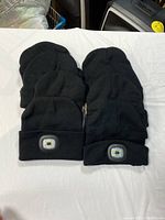 Eight black knit headlamp hats arranged in two stacks of four, showing the front LED light modules clearly visible on some hats.