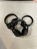 Three black over-ear headphones placed on a white cloth surface, showing overall condition and design.