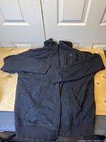 Black heated sweater laid out flat on wooden surface with hood and long sleeves visible.
