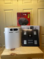 Full view of the three items together placed on wooden surface including the white humidifier, GE bathroom scale in packaging and the boxed Sony CD Radio Boombox.