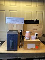 Full lot setup showing FOHERE nut milk maker box, OBERLY milk frother with attachments, pink collapsible kettle, digital timer, white water dispenser, and two black food vacuum sealers.