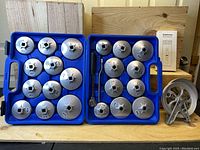 23-piece aluminum filter cap wrench and socket removal set inside blue plastic case, assorted sizes visible, with ratchet tool included, placed on wooden surface.