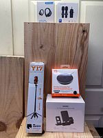 Photo showing Y17 tripod/selfie stick packaging, IQ wireless charging pad box, and Wemiss 3-in-1 phone stand in original packaging, placed on a wooden surface.