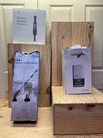 Photo showing the boxed Greenote cordless handheld vacuum, Homtronics 14-in-1 electric cleaning brush, and Healy 1200ml dehumidifier all standing on wooden platforms against a door background.