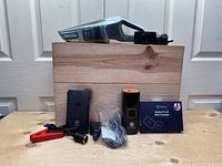 Photo showing handheld vacuum cleaner, Salind 11 4G GPS tracker, Flylinktech car jumper cables, and accessories in front of a wooden crate.