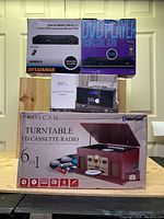 Boxed Proscan 6-in-1 turntable system, Sylvania DVD player box, and Bluetooth CD micro system, stacked and shown from the front.