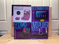Four Proscan media devices in original boxes including 10.1" tablet/DVD combo, 7" and 9" portable DVD players, and progressive scan DVD player.