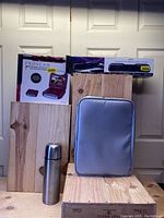 Photo showing Proscan DVD player box, soundbar box, stainless steel thermos, and gray portable locking safe case on wooden surface