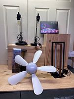 Two Edison bulb bedside lamps with black bases, one white blade ceiling fan with light, box of LED strip lights photographed on table.