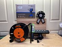 Full lot view showing boxed Wisetool impact wrench, Dewenwils cord reel, Huepar line laser receiver, power bar, and garage lights mounted on wood.