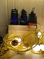 Three Medas submersible water pumps and yellow construction string lights with round white bulbs in a wooden crate.