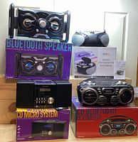 Photo showing entire bundle including Bluetooth speaker with packaging, a radio/cassette boombox, Proscan CD Micro System with packaging and remote, and a black CD Bluetooth Boombox with packaging.