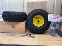 Two new lawn mower pneumatic tires with yellow rims placed on wood planks, includes washers and bushings